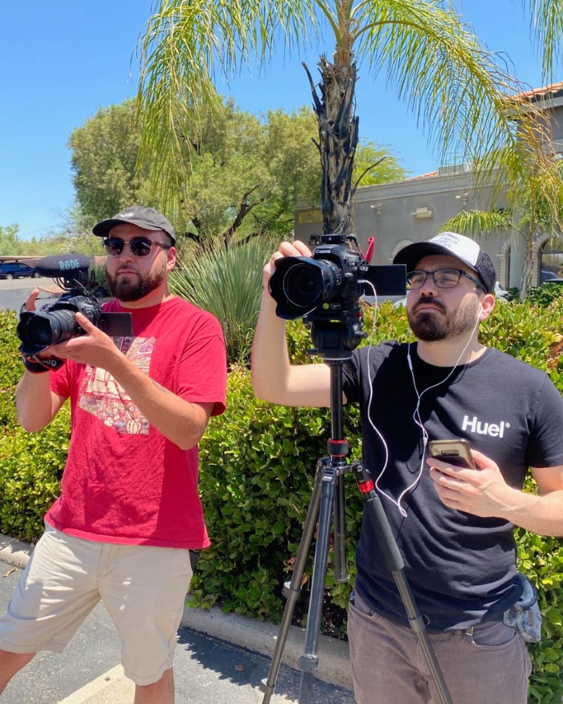 Two Regal Fierce Media crew members filming outdoors with handheld and tripod-mounted cameras